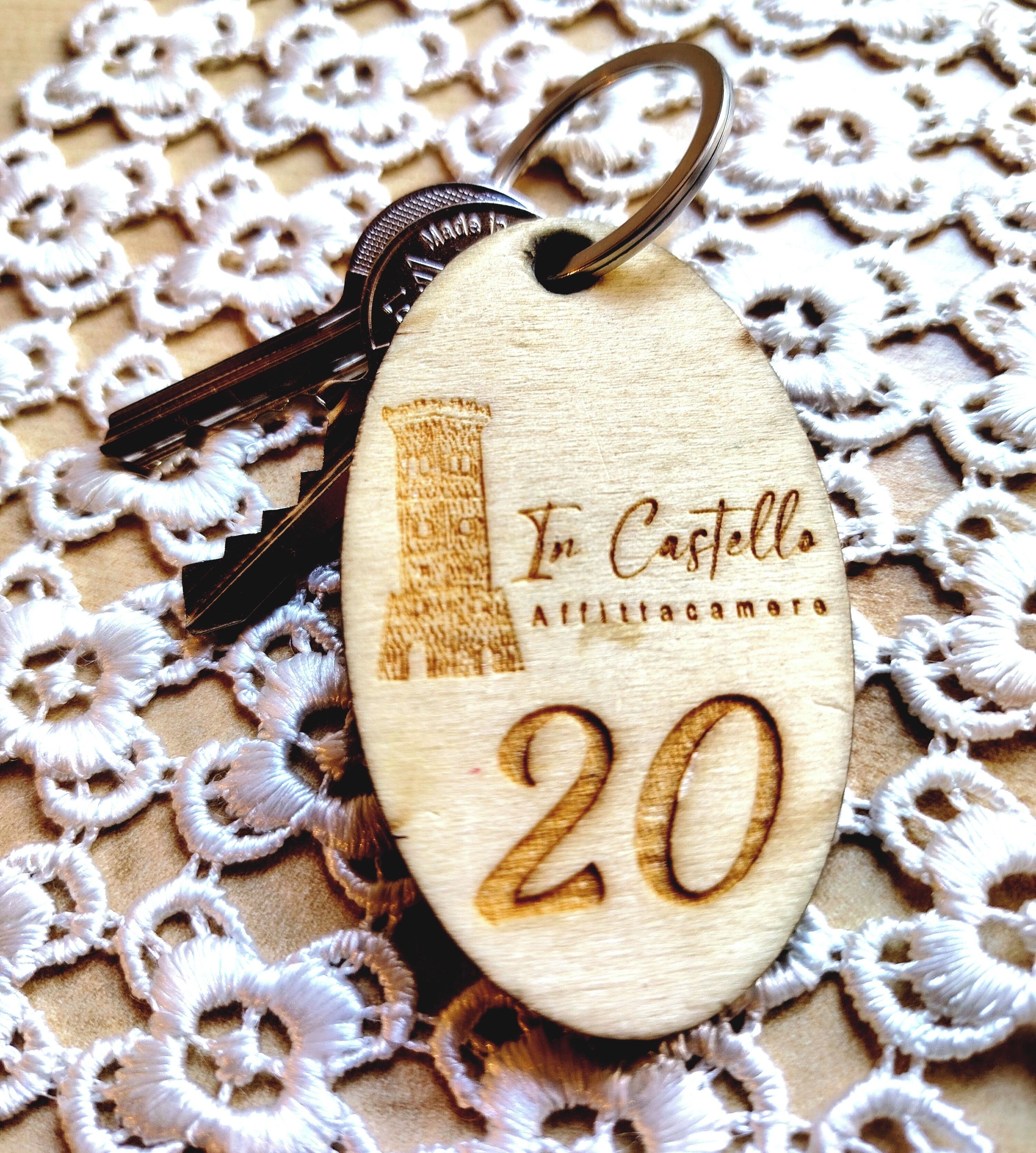A wooden key tag with 'In Castello' and '20' engraved, placed on a lace fabric.