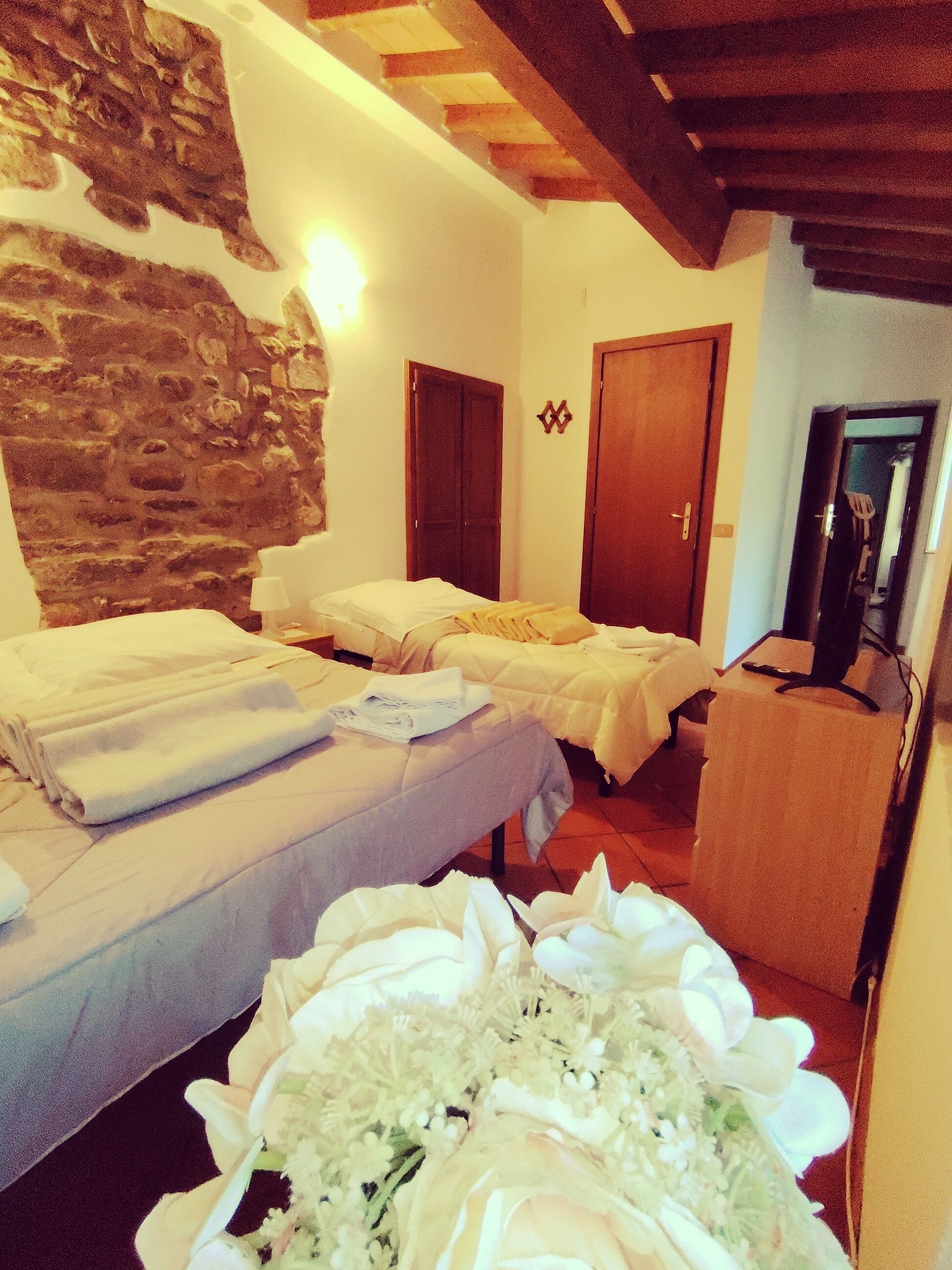 A hotel room with two beds, a stone wall, wooden beams, and a television.
