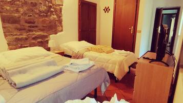 A hotel room with two beds, a stone wall, wooden beams, and a television.