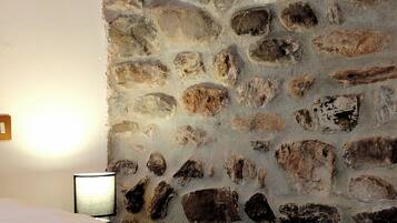 Een kamer met een stenen muur, een bed met een witte dekbedovertrek en een bedlampje.