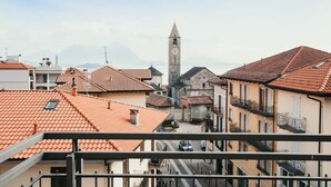 Blick auf eine Stadt mit einem markanten Glockenturm, Gebäuden mit Terrakottadächern und einer Straße mit Autos.