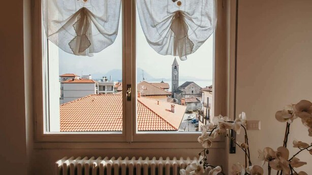 Ein Fenster mit durchscheinenden Vorhängen und Blick auf eine Stadtansicht, darunter ein Glockenturm.