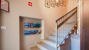 Una escalera con barandilla, un estante fijado a la pared con correspondencia, y un letrero de salida rojo.