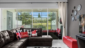 A modern living room with a leather sofa, a red ottoman, and a television. - Mickey's Manor: Private Pool & Resort Access (Davenport)