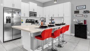A modern kitchen with white cabinets, stainless steel appliances, and red bar stools. - Mickey's Manor: Private Pool & Resort Access (Davenport)