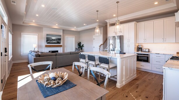 Una cocina moderna con armarios blancos, una isla central y un comedor con mesa y sillas de madera.