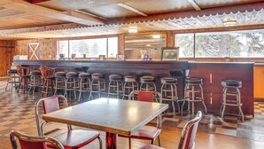 Een restaurant met een geruit vloertje, houten plafond en een bar met krukken.