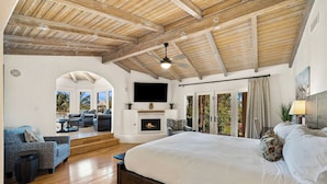 Un dormitorio espacioso con una cama grande, chimenea, televisión y balcón con vistas.