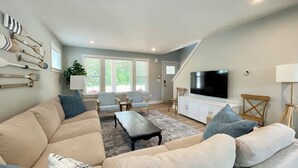 A living room with a sofa, armchairs, a coffee table, a TV, and a staircase. - Northside Cottage. Close to community pool & beaches! Sleeps 12. Fast Wi-Fi! (South Haven)