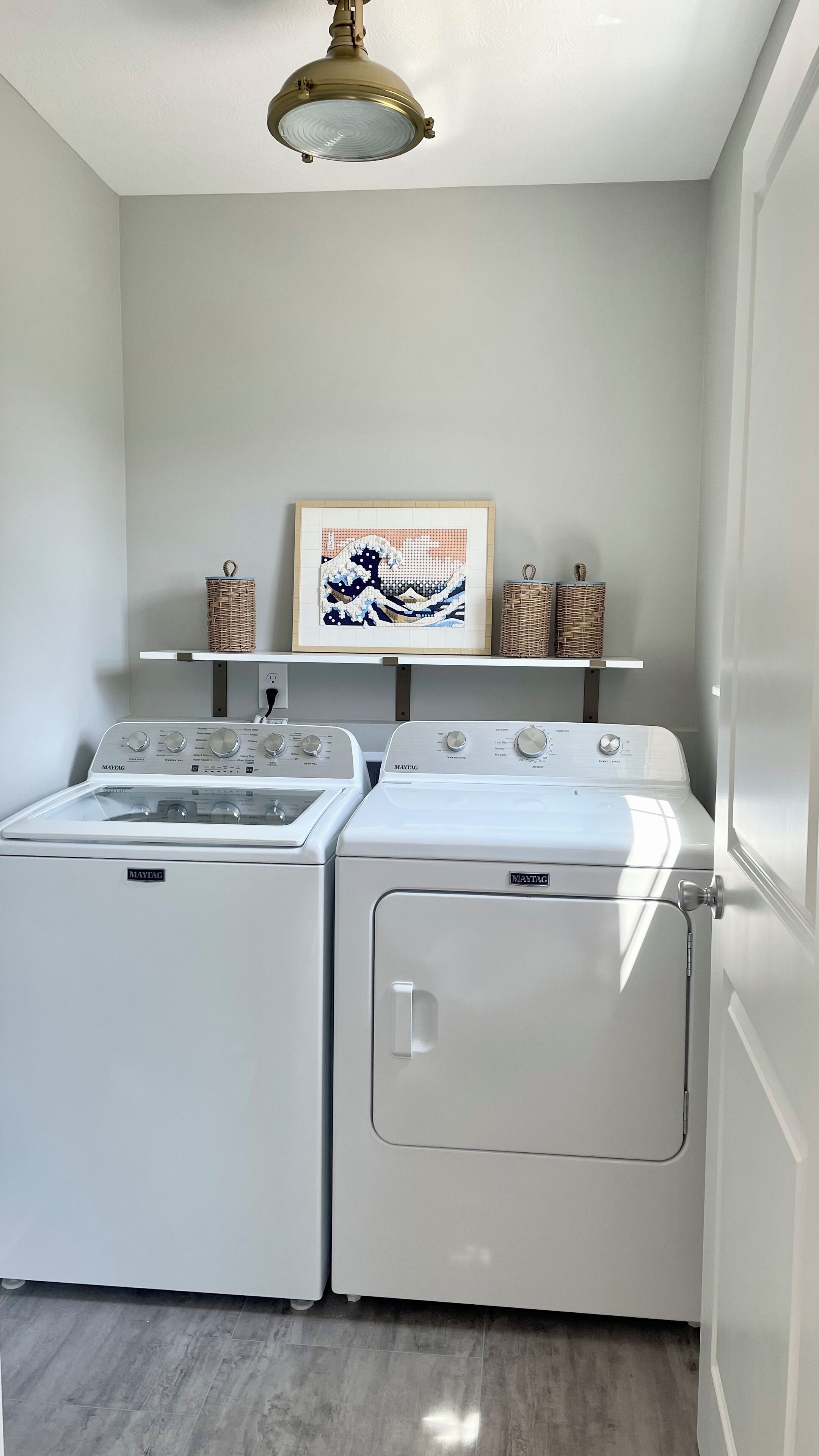 A laundry room with two Maytag washing machines, a ceiling light fixture, and a framed artwork on the wall.