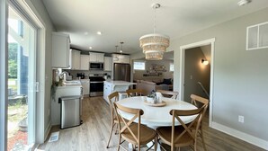 A modern kitchen with white cabinets, stainless steel appliances, and a dining area with wooden chairs and a white table. - Northside Cottage. Close to community pool & beaches! Sleeps 12. Fast Wi-Fi! (South Haven)