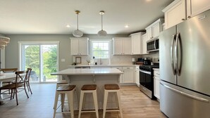 A modern kitchen with white cabinetry, a stainless steel refrigerator, a built-in oven, and a large island with stools. - Northside Cottage. Close to community pool & beaches! Sleeps 12. Fast Wi-Fi! (South Haven)