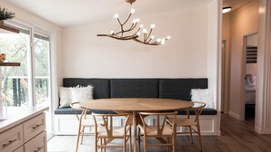 A dining area with a round wooden table, six chairs, a modern chandelier, a bench with cushions, and a view through a window. - The Lookout at Lakewood, Lakefront Paradise with Ultimate Entertainment, Hot Tub and Dock (Bridgeport)
