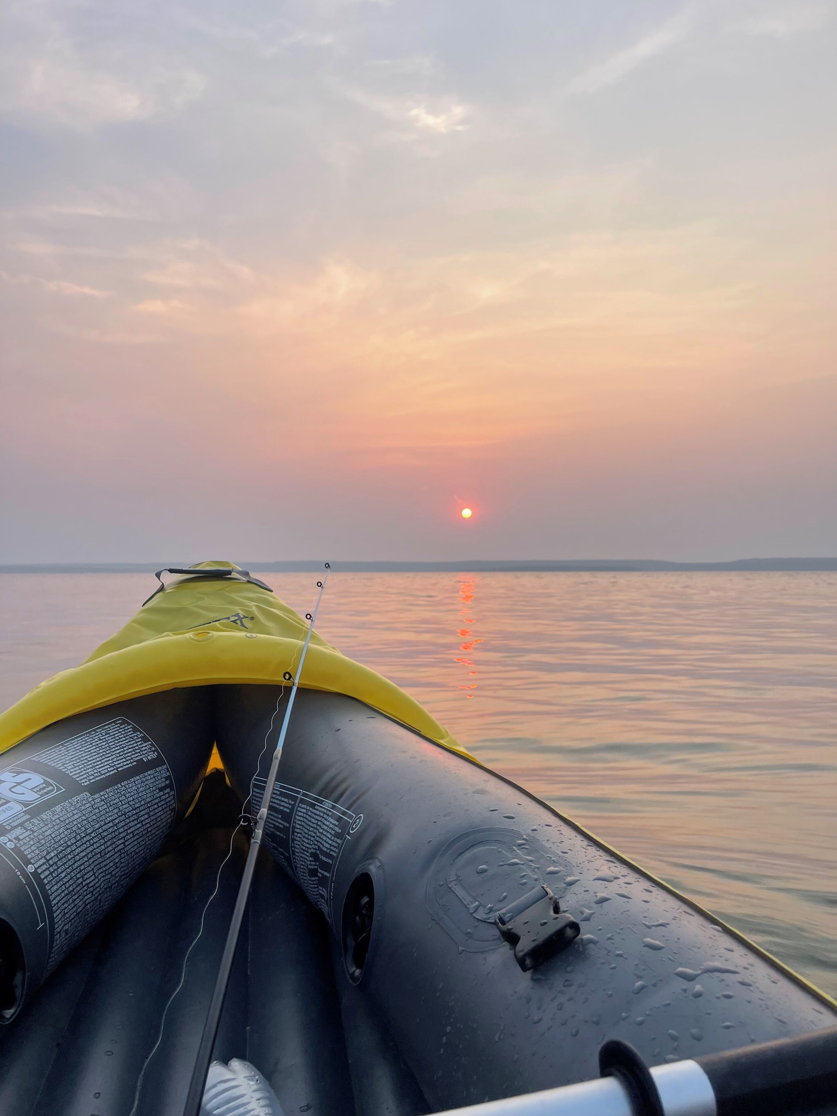 A kayak with a fishing rod on a calm body of water during sunset.