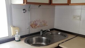 A small kitchen with a sink, a faucet, and a soap dispenser on the counter. There are cabinets with wooden handles and a tiled backsplash with a floral design. - Sandra Home (El Puerto de Santa María)