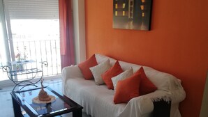A living room with a white sofa, red cushions, a glass coffee table, and white ottomans. - Sandra Home (El Puerto de Santa María)