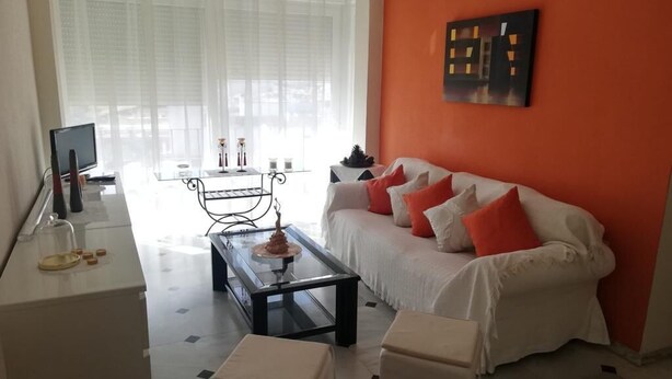 A living room with a white sofa, a coffee table, and a television. - Sandra Home (El Puerto de Santa María)