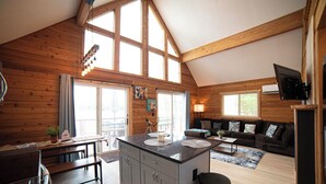 Eine geräumige Hütte mit einer großen Küche, Essbereich und Wohnzimmer. Sie verfügt über Holzwände, große Fenster und eine gemütliche Einrichtung.