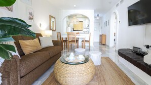 A modern living room with a brown sofa, a glass coffee table with teapots, and a kitchen in the background.