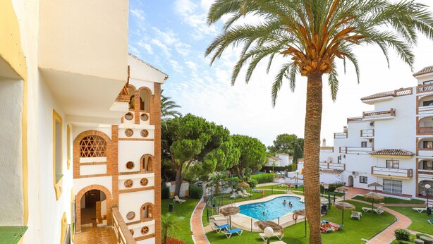 A courtyard with a swimming pool, palm trees, and lounge chairs.