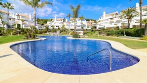 A swimming pool with a tiled edge, surrounded by palm trees and a building complex in the background. - Beachfront with large garden  - Los Monteros Palm Beach (Marbella)