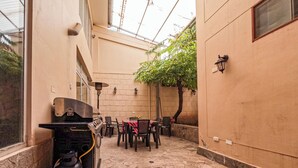A patio area with a barbecue grill, outdoor seating, and a tree. - Pikaflor Cerezo mini apartment (Cusco)