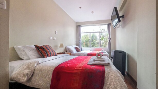 A hotel room with two beds, a TV mounted on the wall, a window with curtains, and a ceiling light. - Pikaflor Cerezo mini apartment (Cusco)