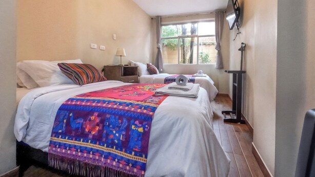 Une chambre d’hôtel avec deux lits, une fenêtre donnant sur la verdure, un téléviseur à écran plat fixé au mur et une table de chevet avec une lampe.