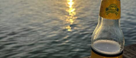 Una botella de cerveza Landshark Island Style sobre una mesa de madera, con vista al atardecer sobre el agua.
