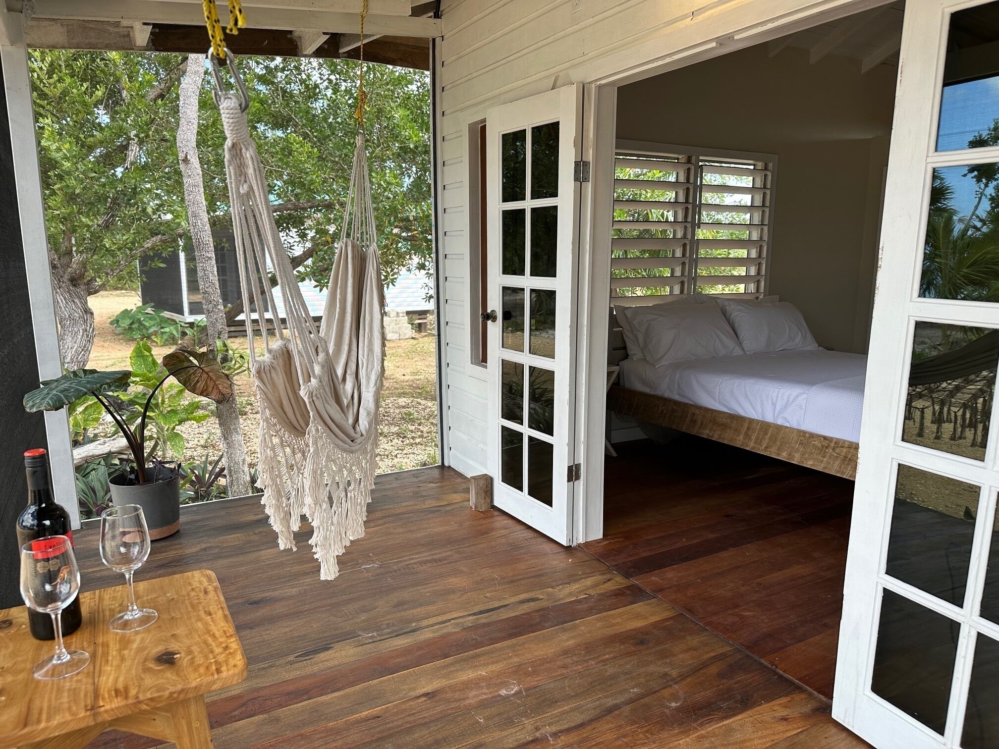 A cozy room with a bed, a wooden table with wine glasses, and macramé hangings.
