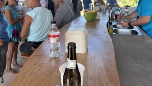 Ein überdachter Essbereich im Freien mit einem Holztisch, einer Bierflasche und einer Wasserflasche.