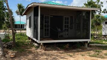 Een gelijkvloers houten huis met een groen dak, een veranda met een schommelstoel en een helder uitzicht over het omliggende landschap.