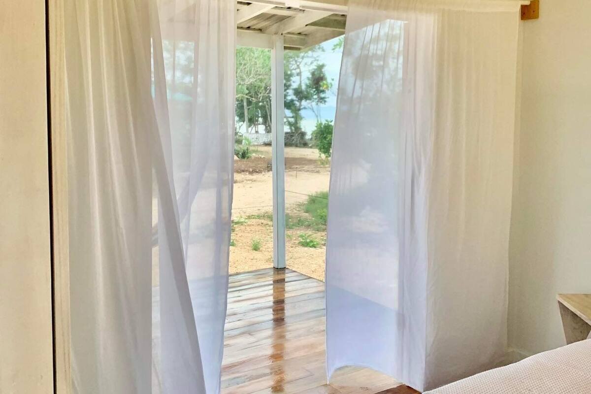 Un dormitori amb sòl de fusta, cortines blanques i vistes a l'exterior.