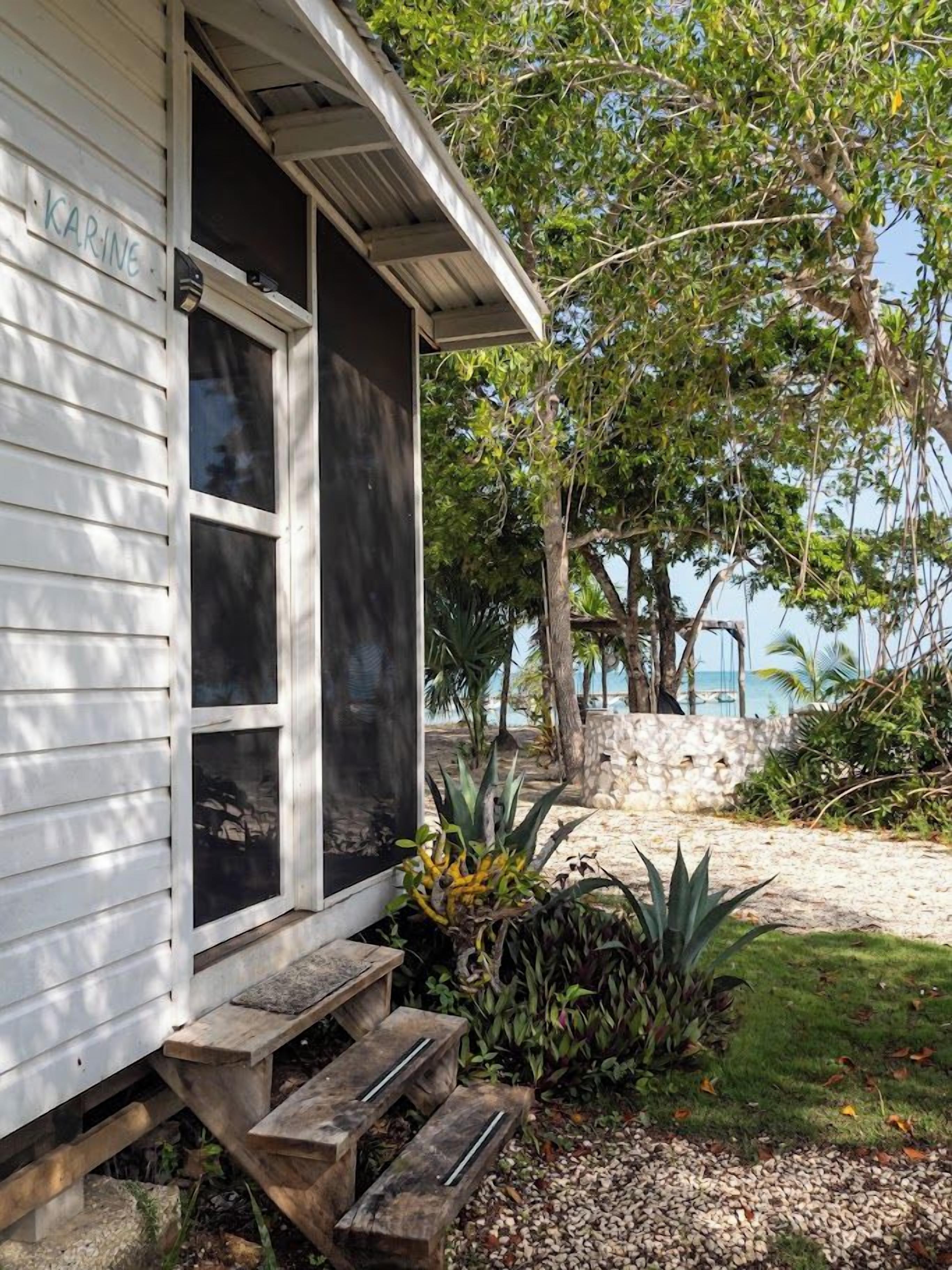 A white building with a nameplate reading 'KARINE' and a wooden staircase leading to a porch.