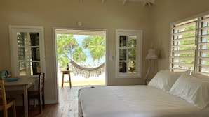 Ein Schlafzimmer mit einem Bett, einem Schreibtisch mit Obstschale und einer Hängematte vor einem Fenster.
