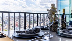 A table set for dining with plates, cutlery, and wine glasses, overlooking a cityscape through a balcony railing. - Piscine  (São Paulo)