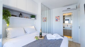A hotel room with a bed, a bedside table with a bottle and glasses, a plant, and a mirror in the corner. - Piscine  (São Paulo)