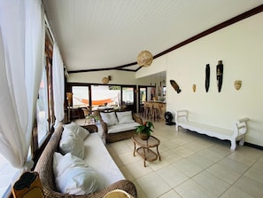 A spacious living area with a sofa, wicker furniture, a fan, and a dining area with a table and chairs.