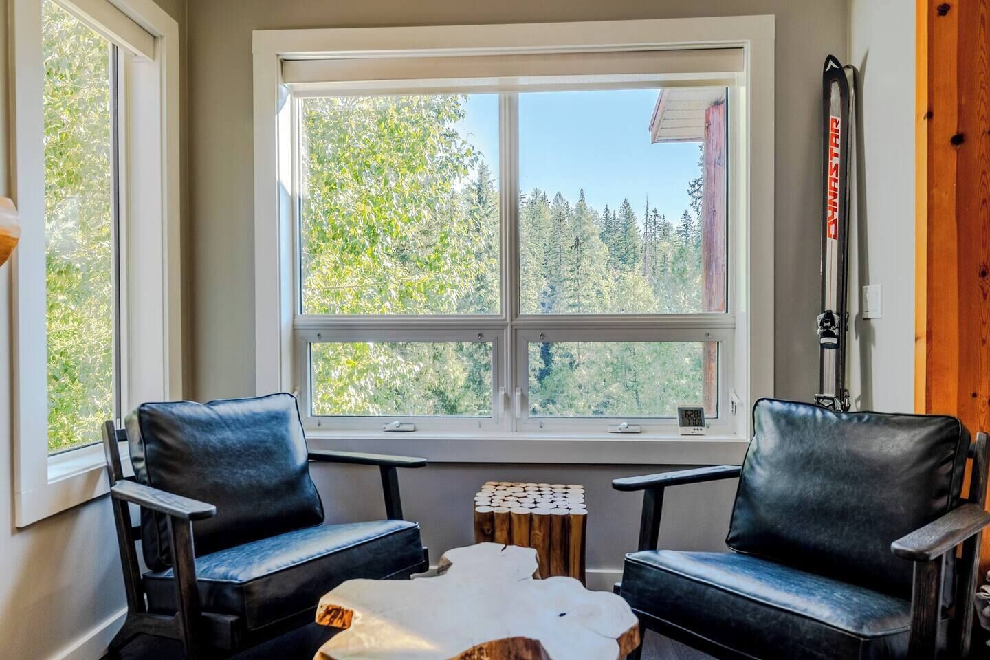 A room with two leather chairs, a small table, and a window with a view of trees.