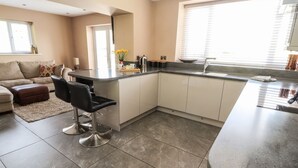 A modern kitchen with a central island, bar stools, and a dining area with a sofa and ottoman. - Pyllau Farm (Llandudno)