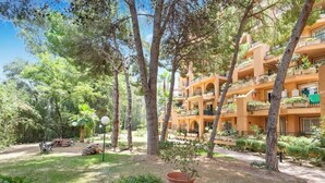 A multi-story building with balconies, surrounded by trees and a grassy area.