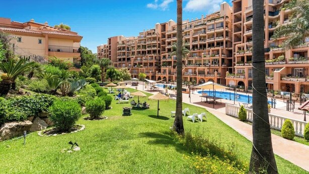 A hotel with multiple balconies, a swimming pool, and lush greenery.