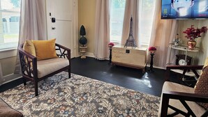 A living room with a ceiling fan, a television, a clock, and a decorative Eiffel Tower model. - Royal European Corner to a Romantic Gateaway by Downtown-Houston, Heights & WOMH (Houston)