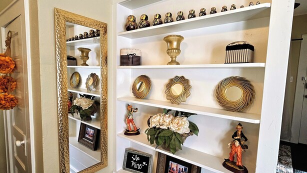 A hallway with a white door, a mirror with a gold frame, and a shelf with decorative items. - Royal European Corner to a Romantic Gateaway by Downtown-Houston, Heights & WOMH (Houston)