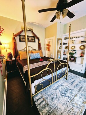 A four-poster bed with a canopy, a ceiling fan, and a decorative mirror on the wall.