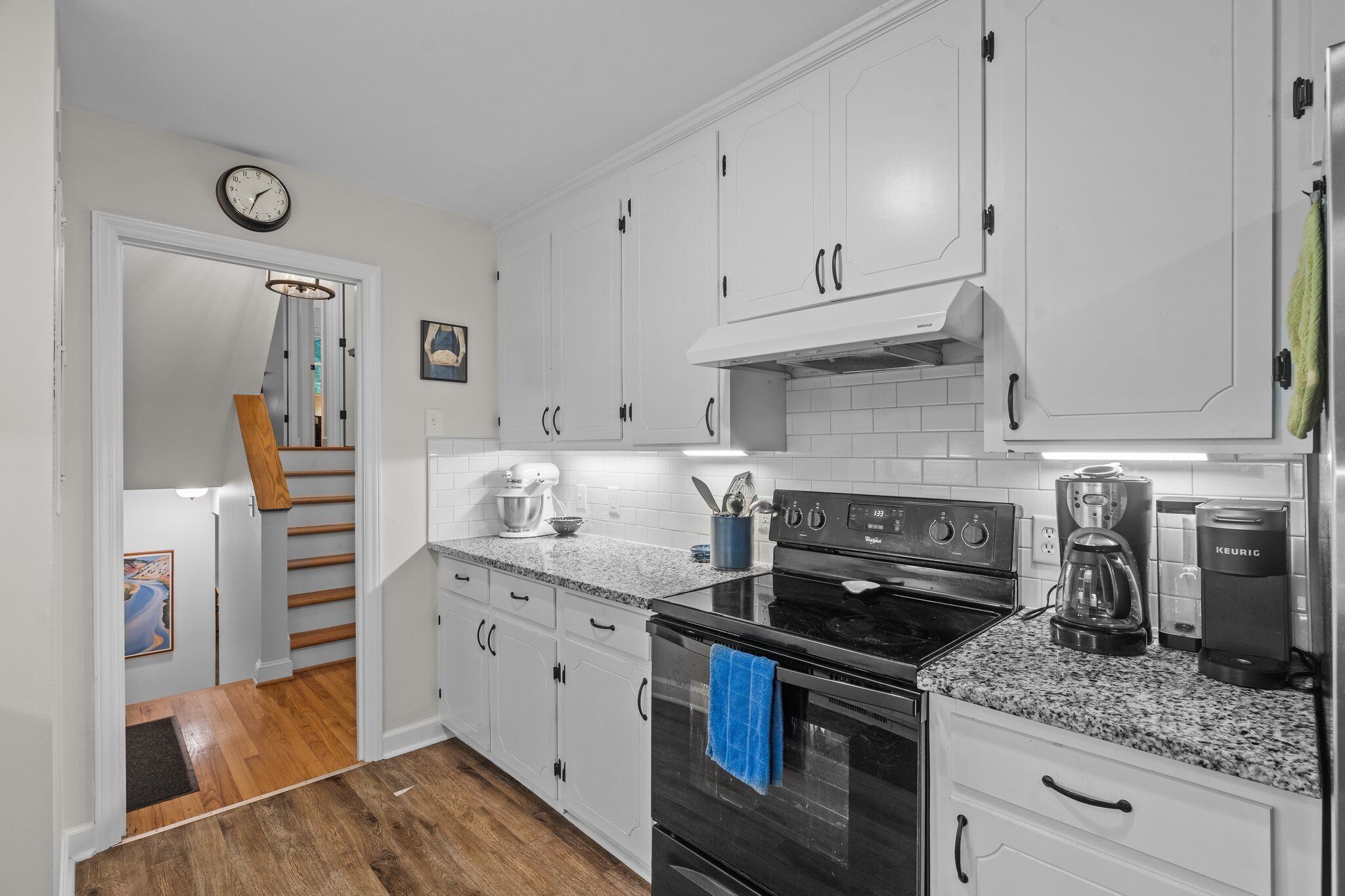 A kitchen with white cabinets, a black stove, a coffee maker, and a clock on the wall.