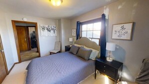 A bedroom with a large bed, a nightstand, a chair, a door, and wall art. - Garfield Park Stay - 5 min to Fountain Square (Indianapolis)