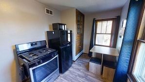 A compact kitchen with a stove, refrigerator, and wooden cabinets. - Garfield Park Stay - 5 min to Fountain Square (Indianapolis)
