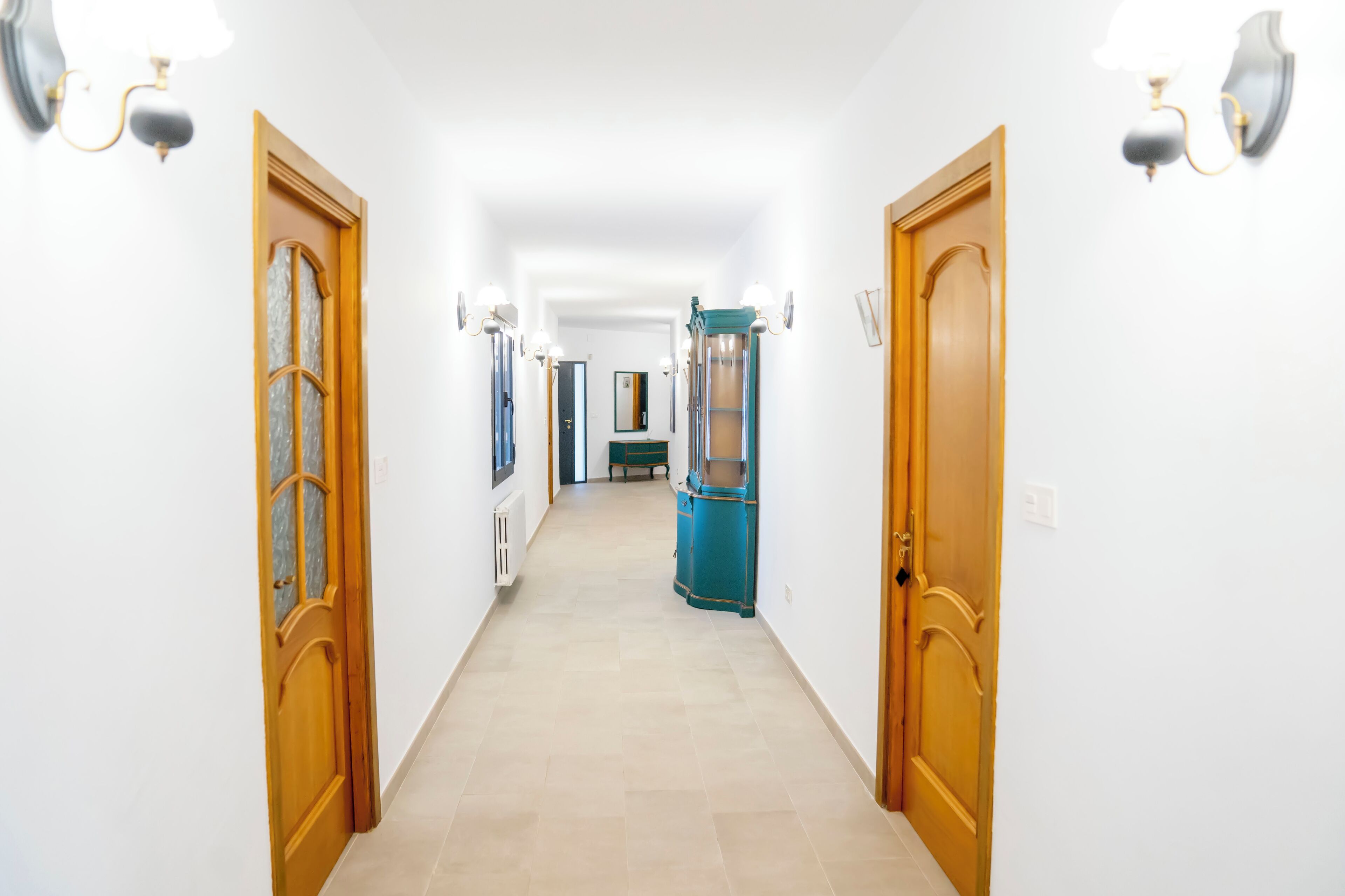 Un couloir avec des portes en bois, une armoire bleue et des appliques murales.