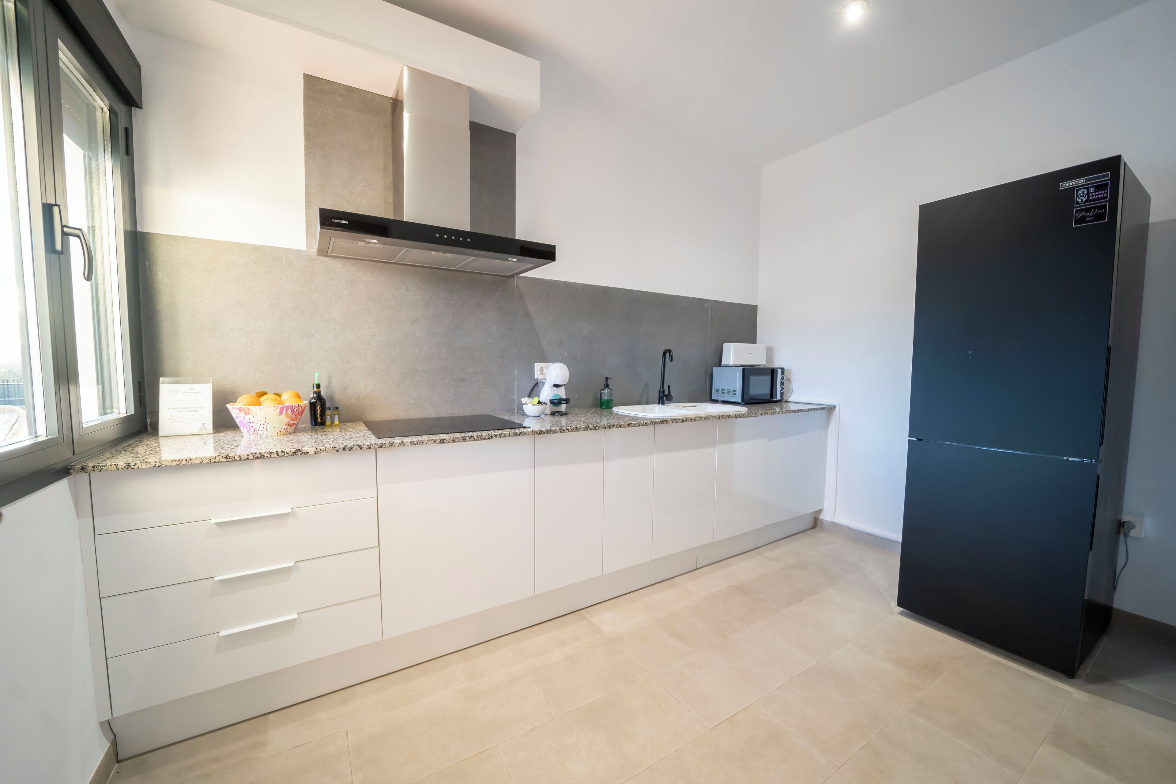 A modern kitchen with white cabinets, a black refrigerator, and a window providing natural light.